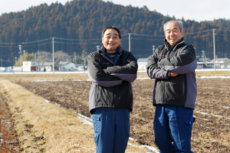 復旧させた農地をバックに微笑む安部社長(右)と佐々木常務(左)