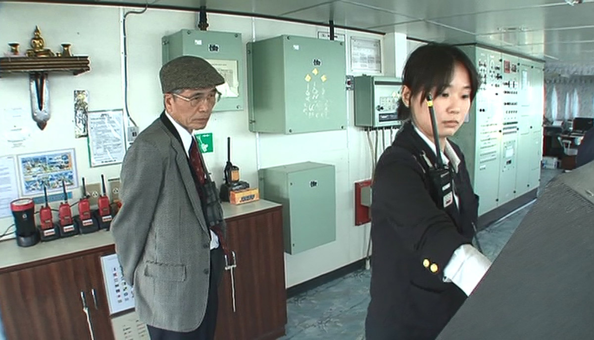 水先人になって1年目、指導水先人の監督下で水先業務を行う西川さん。後ろで指導水先人の目が厳しく光る(画像:「若き海のパイロット」(日本水先人会連合会)より)